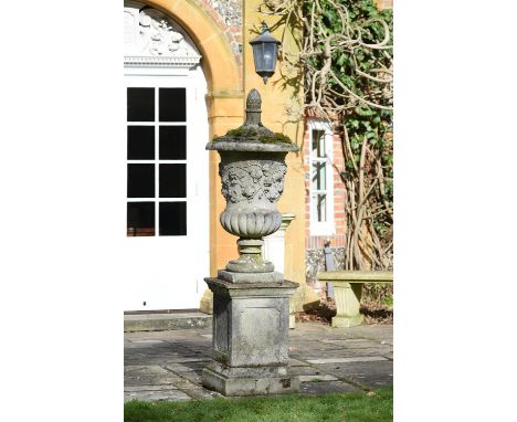 A large stone composition urn on plinth, 20th century, the domed circular cover surmounted by a fircone finial and above a lo