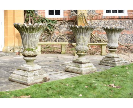 A set of three stone composition garden urns on plinths, 20th century, the fluted and everted bodies loosely of thistle form,