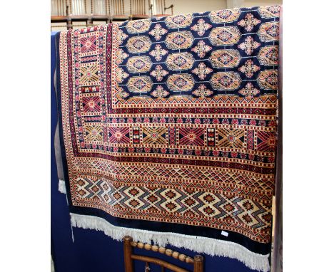 A large 20th Century woollen rug, decorated with red, cream and navy blue geometric patterns on a navy blue ground