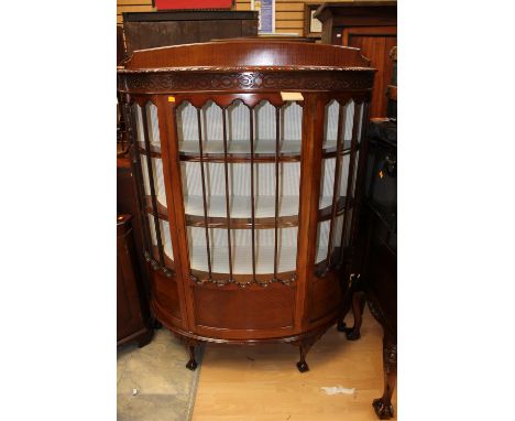 An early 20th Century mahogany bow fronted display cabinet, the glazed door opening to reveal three fitted shelves, raised on