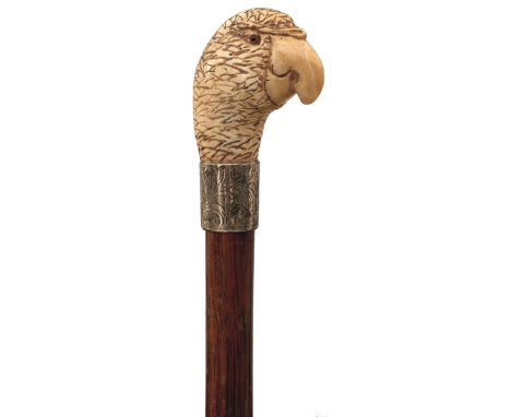 AN EARLY 20TH CENTURY WALKING STICK, the carved ivory handle in the form of a parrot's head with glass eyes, above silver col