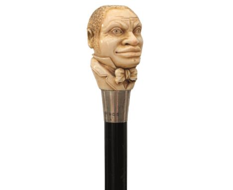 AN EARY 20TH CENTURY JAZZ AGE WALKING CANE, the ivory pommel carved as the head of an Afro-American musician in suit and crav