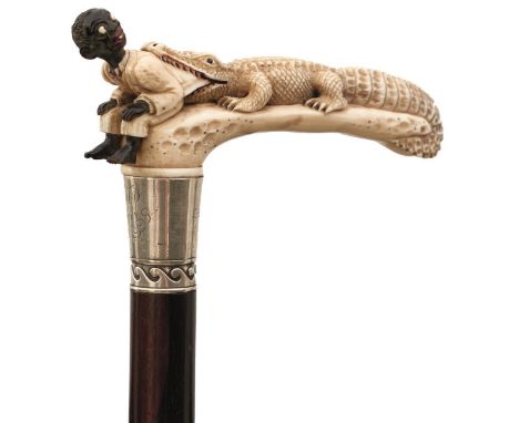 AN EARLY 20TH CENTURY WALKING STICK, the ivory handle carved and stained as a crocodile about to eat a surprised child, the s