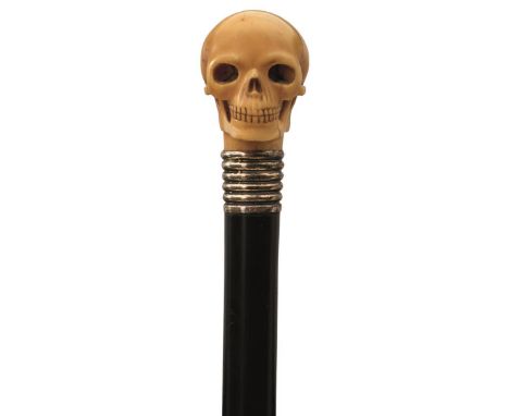 A LATE 19TH/EARLY 20TH CENTURY WALKING STICK, the ivory handle carved in the form of a skull, above ribbed silver collar with