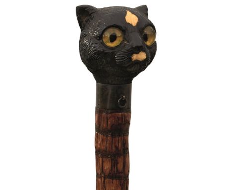 A VICTORIAN WALKING STICK, the carved and ebonised wood and ivory handle in the form of a cat's head with green and yellow gl