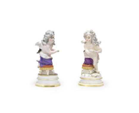 Two Meissen figures of Cupid, late 19th centuryModelled by Heinrich Schwabe, each wearing a long wig, cloak and pince-nez and