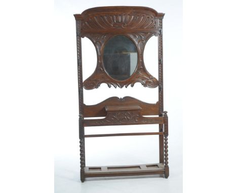 A Late Victorian carved oak hall stand
The scrolling leaf carved back centred with an oval mirror above a hinged glove box an