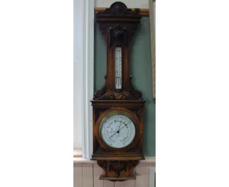 An Edwardian oak wall barometer with profusely carved case with heraldic shields and carved eagle surmounting the thermometer