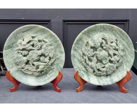 A large pair of Chinese carved mottled green jade relief chargers, decorated with dragons, 35cm diameter,&nbsp;on folding sta