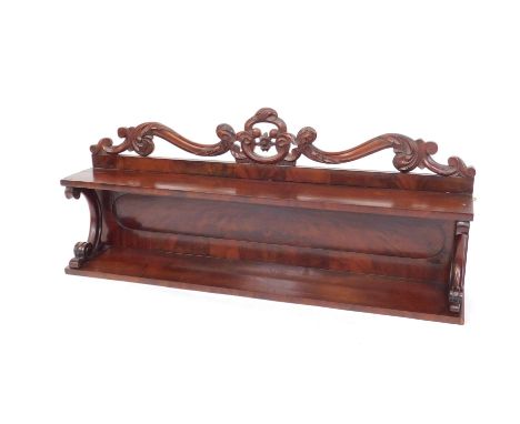 A Victorian mahogany wall mounted bookshelf, with a leaf and floral carved scroll top, above a single shelf, raised on scroll