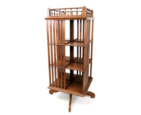 A late Victorian light oak square revolving four tier bookcase, with galleried top and slatted sides, on a scrolled quadripar