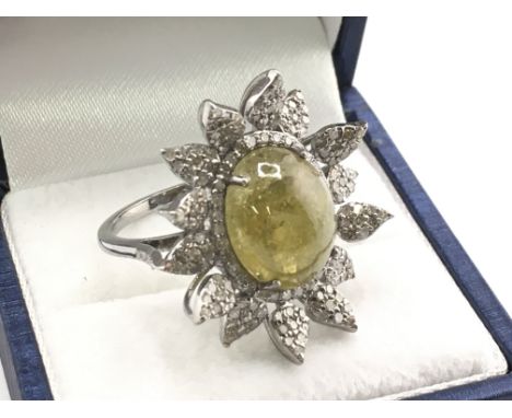 A floral style ring set with a central oval cabochon green tourmaline, with surrounding diamond-set leaves in white metal. To