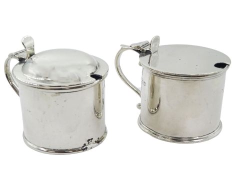 Two early 20th century silver mustard pot and covers, each of plain drum form, the first example with domed cover, hallmarked