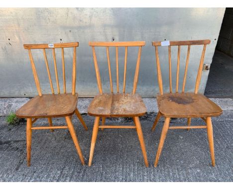 Three Ercol beech dining chairs, each with stick back and shaped seats, stamped mark to base 884923, green and gold label