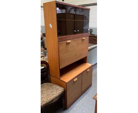 A mid-20th century G Plan style unit, with pair of smoked glass doors to the top, opening to a single loose shelf, below this