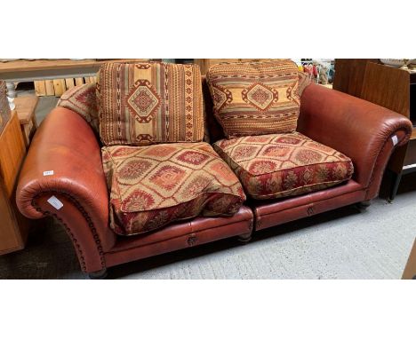 A 20th century two seat sofa, with red leather covered frame and stud decoration, the seats and back upholstered in a heavy g