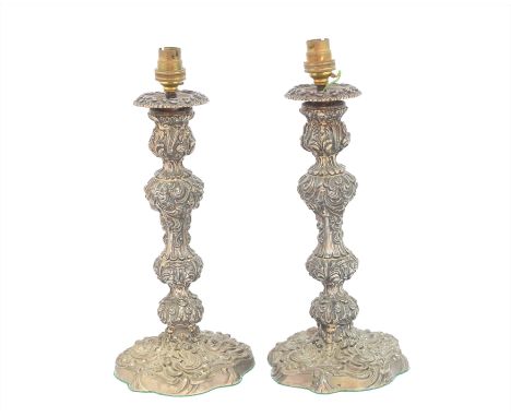 A pair of Georgian silver candlestick lamp bases, each designed with repoussé scrolling and acanthus decoration, and circular