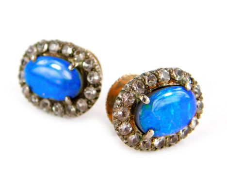 A pair of opal and paste stone earrings, the oval central stone surrounded by white stones in claw setting, in a white metal 