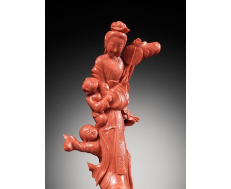 A CHINESE CARVED RED CORAL FIGURE OF A MEIREN WITH BOYSChina, early to mid-20th century. The tall beauty is finely carved sta