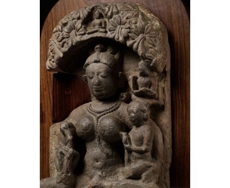 A SANDSTONE STELE OF AMBIKA, INDIA, 11TH-12TH CENTURYSeated beneath a floral canopy with a central Buddha figure, the goddess