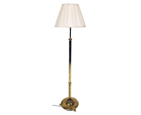 An early 20thC brass floor lamp, of cylindrical form on a circular base with three moulded feet, and a shade, 175cm high. and