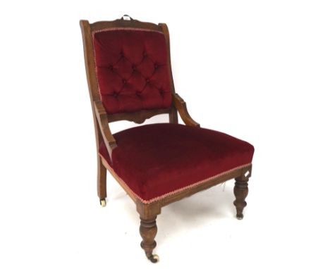 An early 20th century button back elbow chair, upholstered in red velvet, the wooden frame with carved details, raised on tur