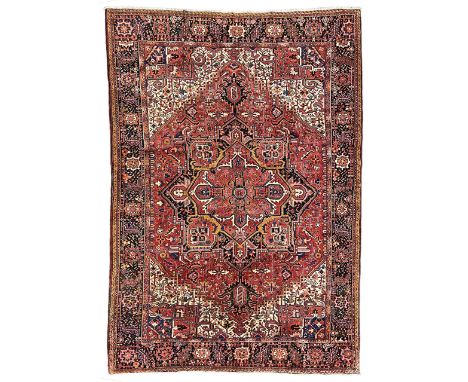 Persian Heriz crimson ground carpet, the field decorated with a central floral medallion surrounded by geometric stylised pla