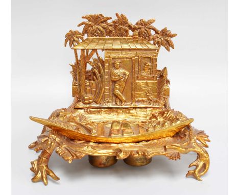 A Novelty Gilt Metal Desk Stand, formed as a riverside shack with a sailor and a native figure, the letter rack formed as pal