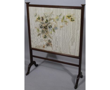 An Edwardian mahogany firescreen, with embroidered centre decorated with pansies, before a plain back on scroll feet, 86cm hi
