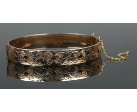 A 9ct rolled gold hinged bangle, set with four garnet stones and half engraved detailing.  Safety chain snapped.