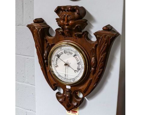 A Victorian carved oak aneroid barometer, circa 1890, shield form case with a central carved mask, 56cm high, 49cm wideThe ca