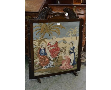 A Victorian woolwork firescreen, hand stitched with a Biblical scene, The Flight of Mary, Joseph and The Infant Jesus, carved