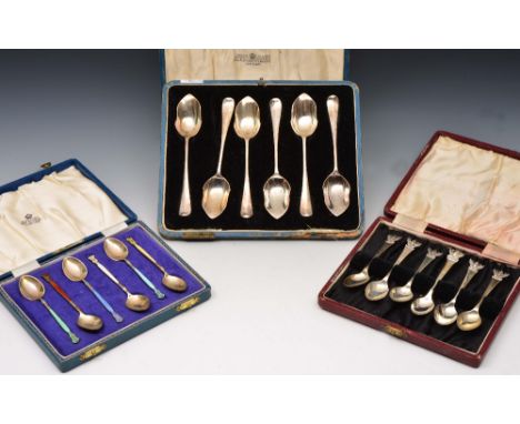 Three cased sets of silver spoons including one set with shaped finials and another set with coloured enamel decoration