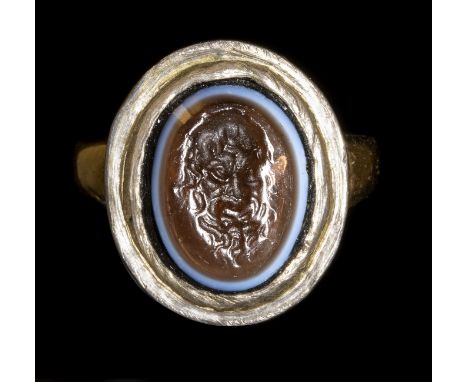 A GLASS IMPRESSION SET IN A GOLD RING. MASK OF A FAUN.18th centuryGlass 10x12 mm; Int. Size 14,5x15 mm; 4,17 grA three layers