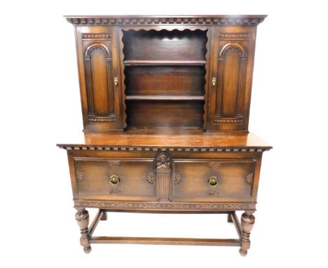 An oak dresser, the top with a dentil cornice above two carved panelled doors flanking two plate shelves, the base with an ar