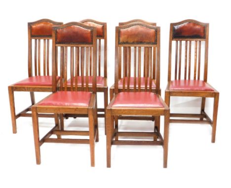 A set of six Edwardian oak dining chairs, each with a red leatherette padded back with button borders, and a later red leathe
