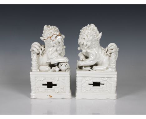 A pair of Chinese blanc de chine porcelain Foo Dogswith incense stick holders, on plinths, 20.5cm. high. (2)