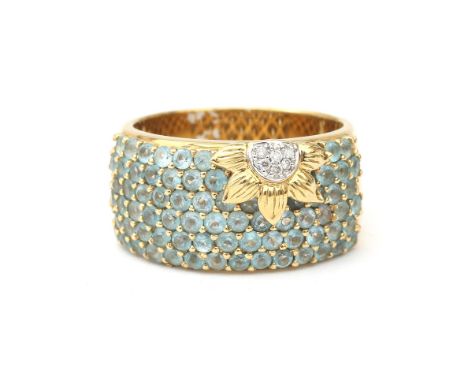 An 18 karat gold ring with topaz and diamond. The front is pavé set with light blue topaz featuring a diamond set flower at t