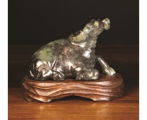 A Spinach Jade Carving of a Reclining Water Buffalo mounted on a  carved wooden stand. The buffalo 5 ins (13 cms) high, 8 ins