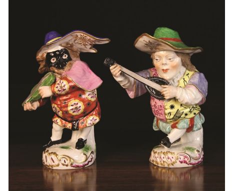 A Pair of Porcelain Mansion House Dwarfs dressed in flamboyant hats and costume; one playing a fiddle, the other a lute, stan