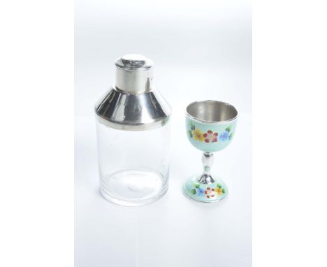 A silver mounted glass tea caddy and an enamelled white metal egg cupThe caddy with a removable cap over a cylindrical glass 