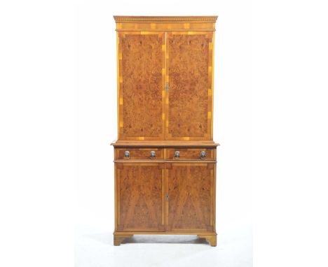 A reproduction yew wood drinks cabinetwith a dentil cornice above two cupboard doors enclosing a mirrored interior over two f
