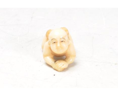 An early 20th Century Japanese carved ivory netsuke figurine in the form of a crawling child / baby in traditional clothing, 