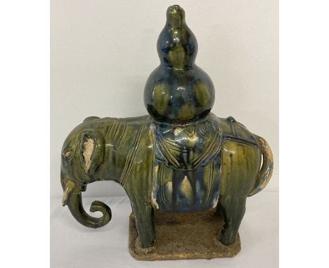 A stoneware ceramic elephant figurine carrying a gourd, in blue/green majolica style glaze. Approx. 33cm tall x 28cm long.