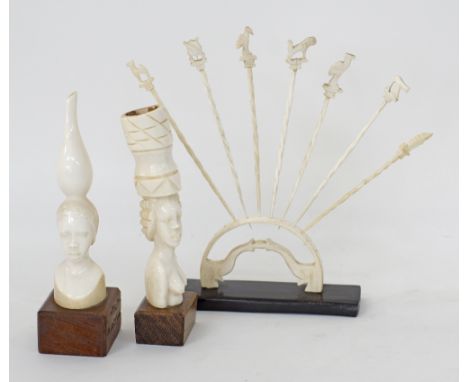 An African stand with seven ivory cocktail sticks, together with two ivory busts of women carrying cauldrons on their heads, 