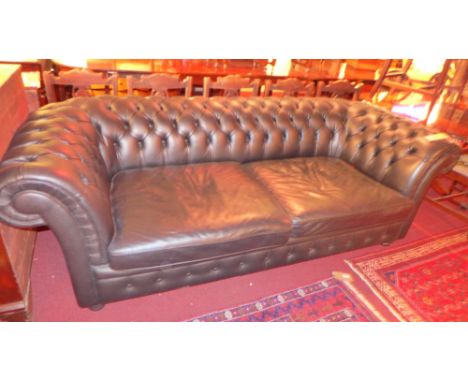 A contemporary designer Chesterfield three seater sofa upholstered in black buttoned leather raised on ebonised bun feet