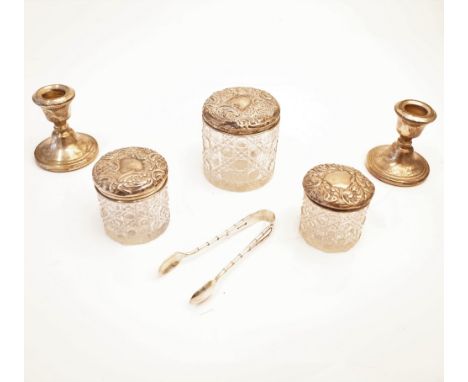 Three silver lidded faceted glass toilet jars, with embossed decoration, a pair of silver small candlesticks (loaded), Birmin