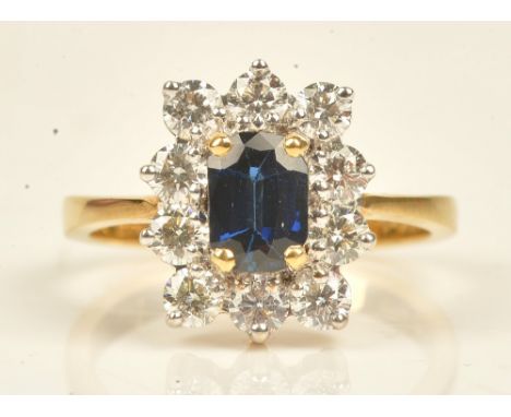 A gold, sapphire and diamond eleven stone cluster ring, claw set with the cushion shaped sapphire at the centre, in a surroun