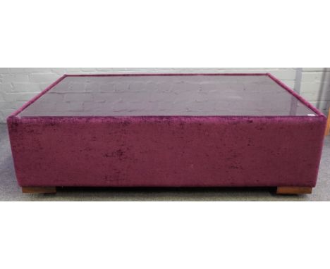 A large square plum coloured upholstered coffee table, with inset glass top on block supports, 130cm wide x 42cm high.