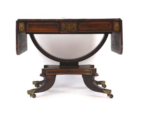 A Regency rosewood and brass inlaid sofa table on a U-shaped support, platform base and for splayed legs with brass caps and 